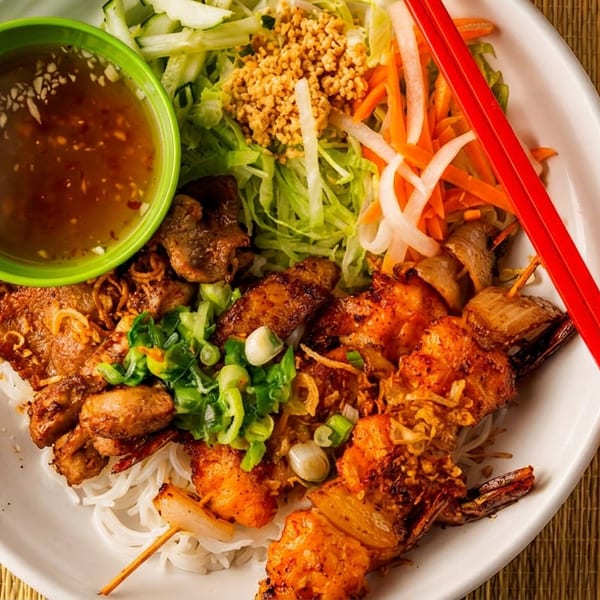 A vibrant Vietnamese vermicelli bowl with grilled shrimp, pork, fresh vegetables, and dipping sauce.